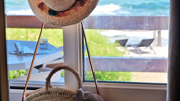 Un panier tressé est suspendu près d’une fenêtre, d’où l’on a vue sur l’océan, et des chaises de plage sont disposées à l’extérieur.