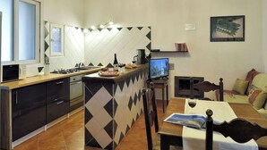 Une cuisine compacte dotée d’un îlot central, un coin repas avec une table et des chaises, et un espace de vie comprenant un canapé et un téléviseur.