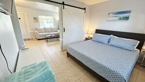 A bedroom with a bed, a desk, a chair, a ceiling fan, and a view of the living area. - Private 1/1 Poolside Cottage! BBQ Grills, Near Beach & More! (Fort Myers)