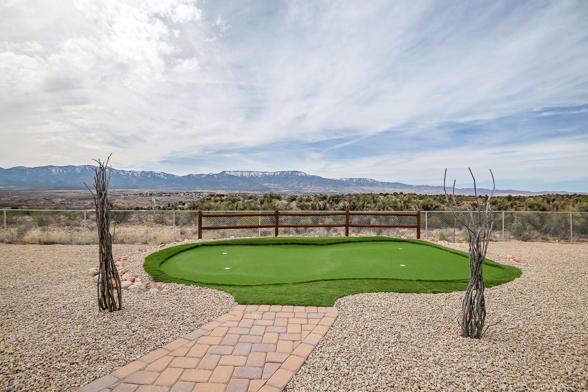 Un campo de golf con un banco de madera, un putting green y vistas de montañas al fondo.