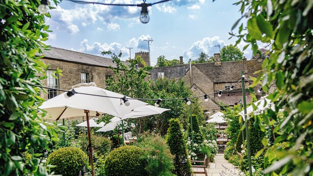 An outdoor patio area with umbrellas, potted plants, and stone buildings in the background. - Cozy Cotswold Dog Friendly Retreat  (Northleach)