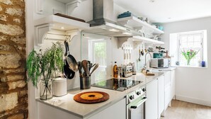 A modern kitchen with white cabinetry, a built-in oven, a microwave, and a stove. There is a window with a view of greenery outside. - Cozy Cotswold Dog Friendly Retreat  (Northleach)