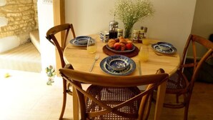 A dining area with a wooden table, four chairs, a wall clock, and a vase with flowers. - Cozy Cotswold Dog Friendly Retreat  (Northleach)