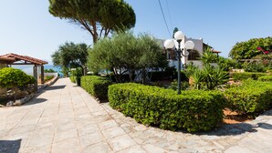 A stone pathway leading to a white building with a red roof, surrounded by well-maintained hedges and a large tree. - Seaside Family Villa for Weddings and Ceremonies (Rethymno)