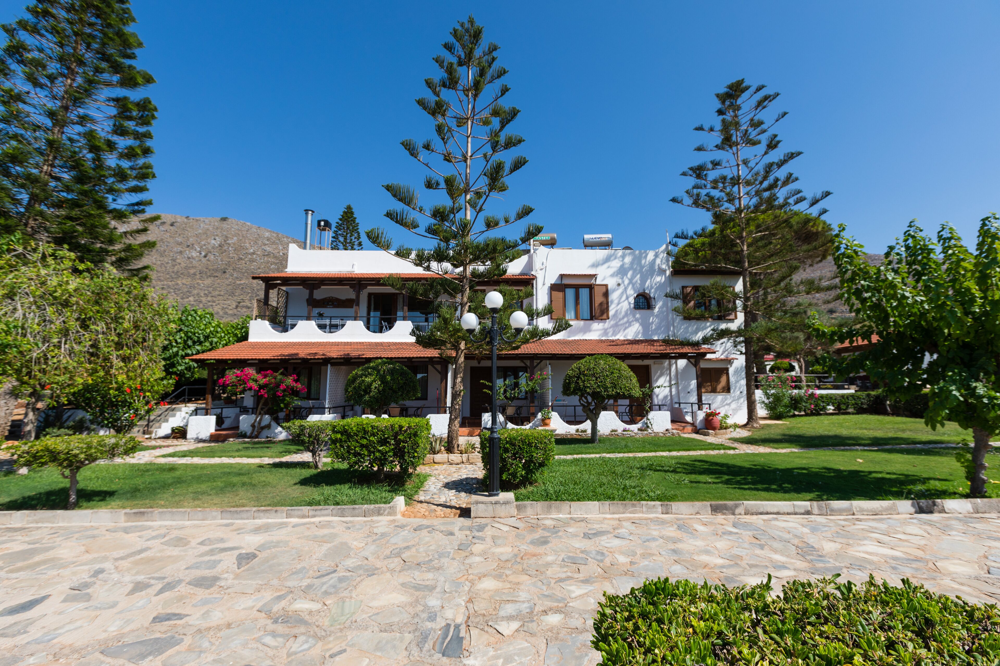 A two-story building with a stone-paved courtyard, surrounded by greenery and trees.