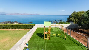 A children's play area with a swing set and a slide, overlooking a body of water. - Seaside Family Villa for Weddings and Ceremonies (Rethymno)