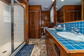 A bathroom with a glass shower enclosure, wooden cabinets, a blue-tiled sink, and a toilet.
