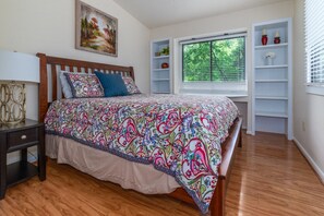 A bedroom with a wooden bed, a bedside table, a window with blinds, and built-in shelving with decorative items. - Riverside Cottage with 2 Kayaks & Canoe (Lexington)