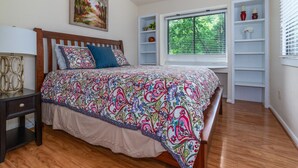 Un dormitorio con cama de madera, una mesita de noche, una ventana con persianas y estanterías empotradas decoradas con objetos.