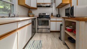 Una cocina compacta con gabinetes blancos, electrodomésticos de acero inoxidable y un tragaluz.