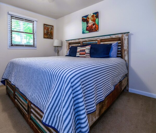A bedroom with a bed, a window with blinds, a painting on the wall, and a lamp. - Riverside Cottage with 2 Kayaks & Canoe (Lexington)