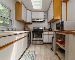 A compact kitchen with white cabinets, stainless steel appliances, and a skylight. - Riverside Cottage with 2 Kayaks & Canoe (Lexington)