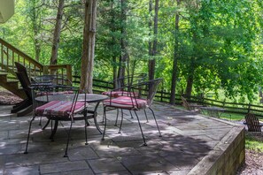 An outdoor patio with a table and chairs, surrounded by a wooden deck and a stone floor.