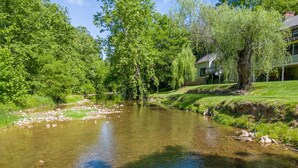 Een heldere rivier met bomen en een huis op de achtergrond.