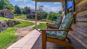 Een houten veranda met twee stoelen, een pad van stenen en ruime blokhutten op de achtergrond.