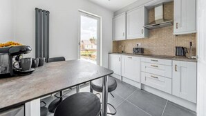 Ett modernt kök med vita skåp, ett matbord och en kaffemaskin.