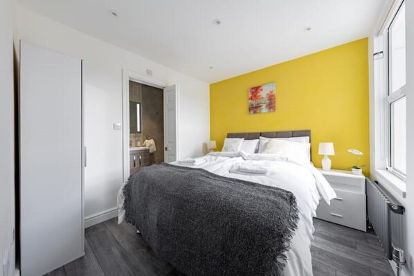 A bedroom with a bed, a nightstand, a lamp, and a window. - Viti Levu House (Southall)