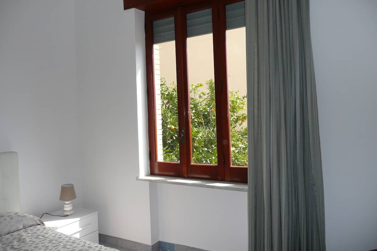 A bedroom with a window, a bedside table, and a lamp.