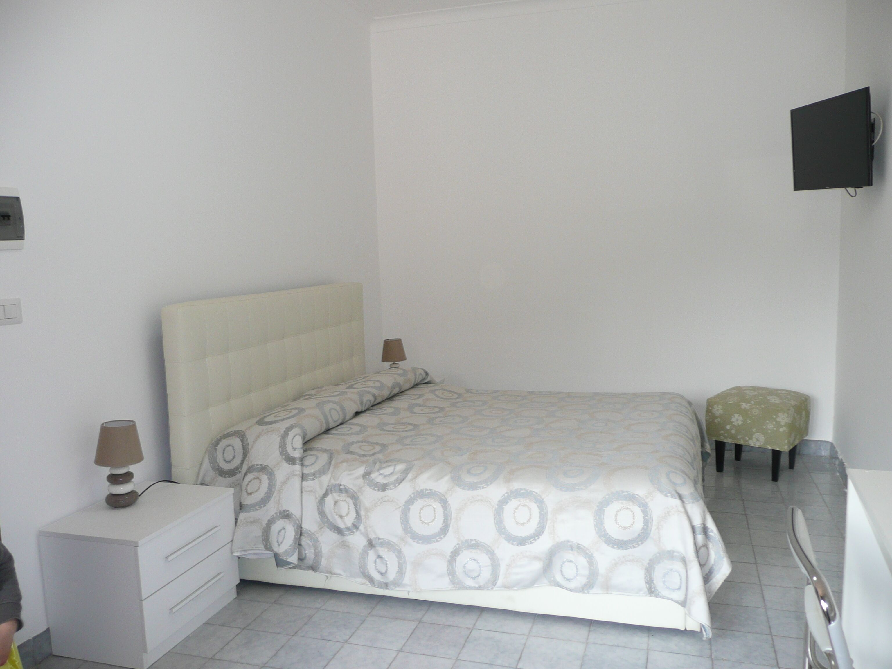 A bedroom with a bed, a bedside table, a lamp, a TV, and a small stool.