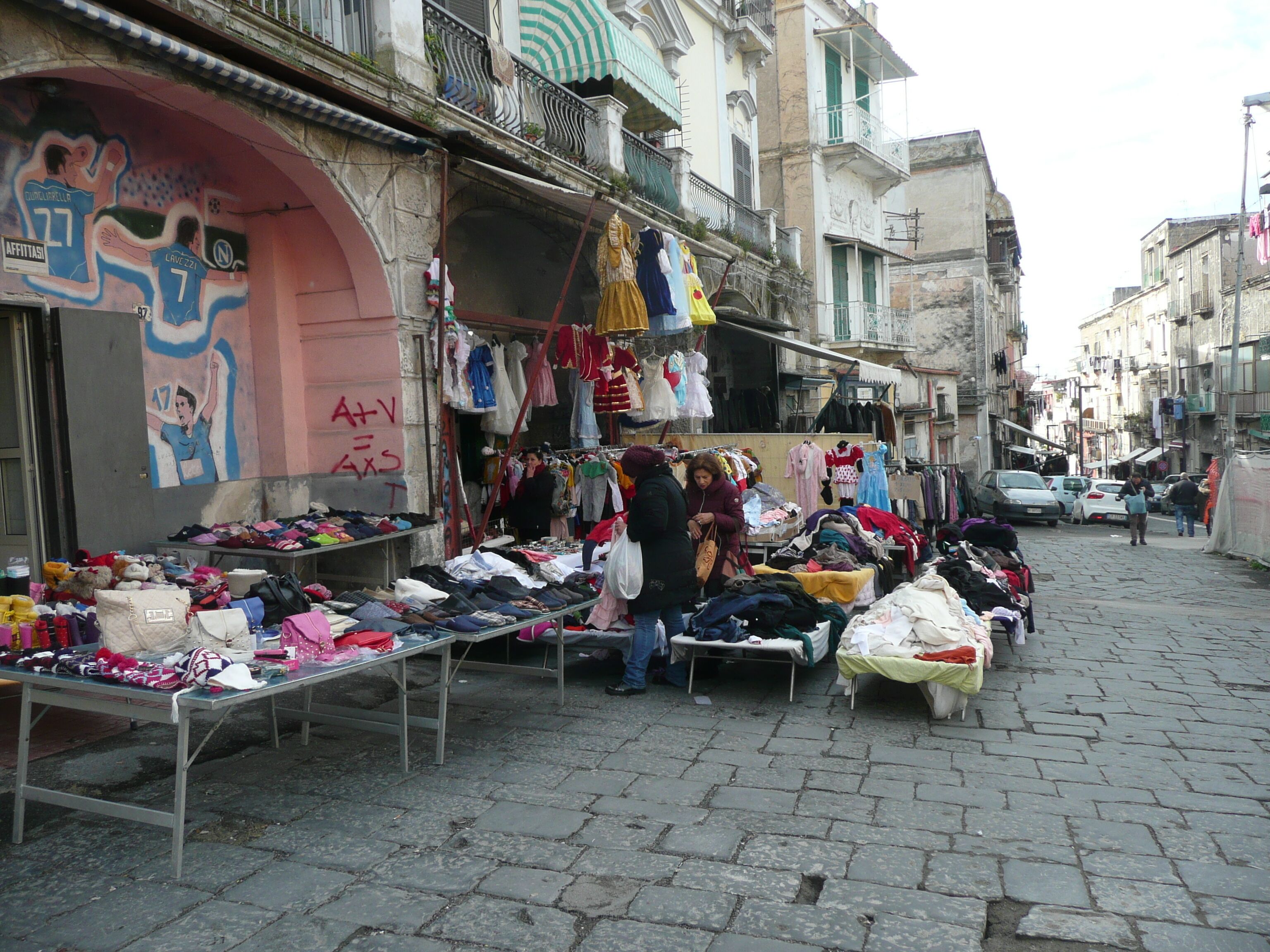 A street market with various stalls selling clothes and accessories.