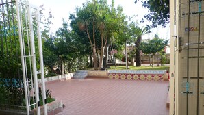 Un patio empedrado con un borde de baldosas, rodeado de árboles y una reja de metal.