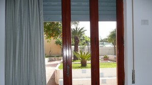 Una habitación con un ventanal grande, una puerta de madera y vista a un jardín con una palmera y un árbol pequeño.