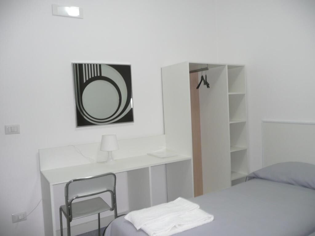 Un dormitorio moderno con cama, escritorio con silla, armario y espejo en la pared.