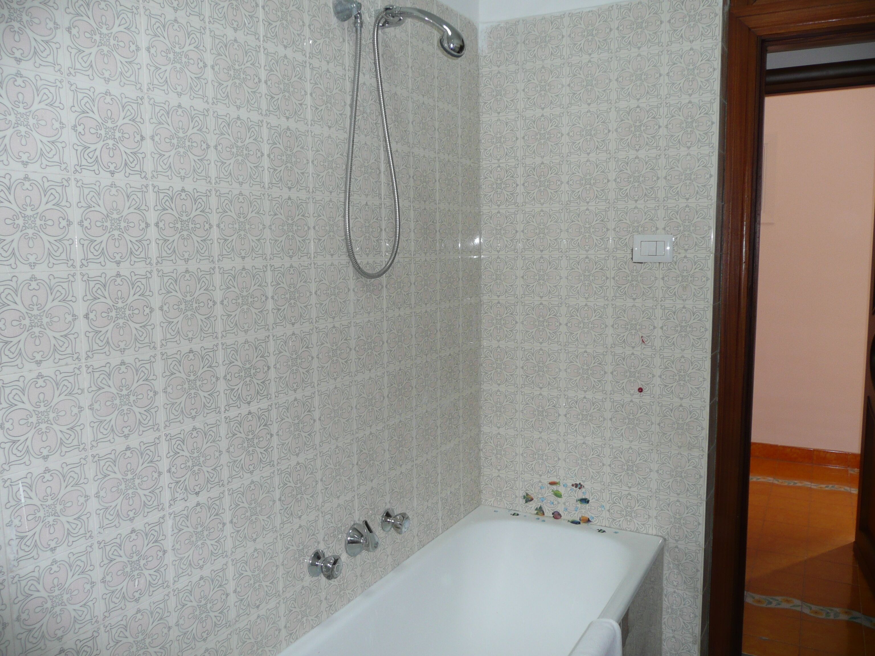 Une salle de bain avec une baignoire, une douche et des toilettes. Les murs sont recouverts de carreaux décoratifs.