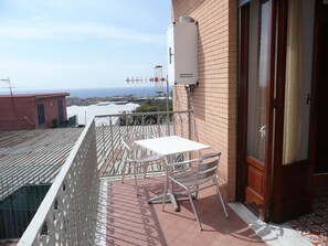 A balcony with a white table and chairs, a view of the sea, and a brick building. - GARDEN HOUSE ERCOLANO (Ercolano)
