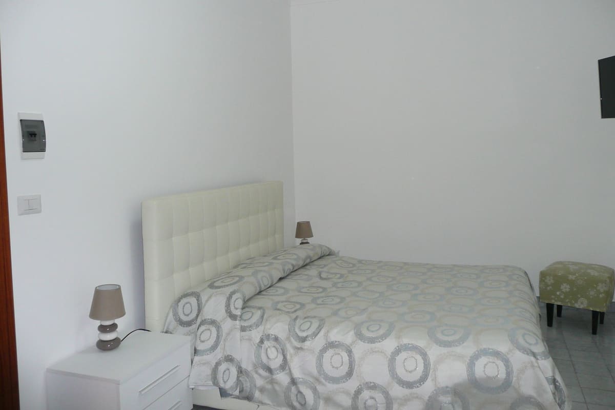 A bedroom with a bed, a bedside table, a lamp, and a small stool.