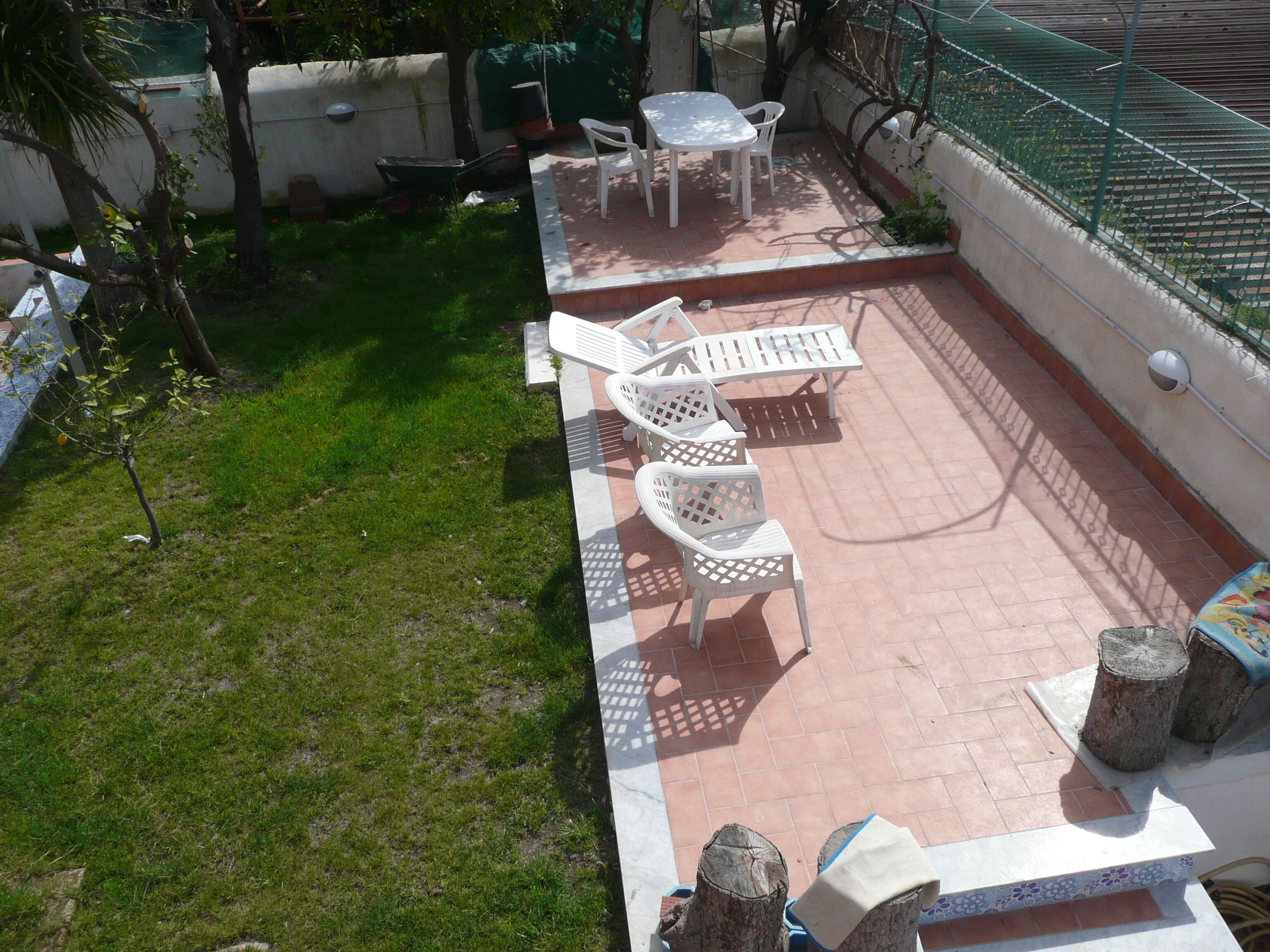 Un espace patio avec une table et des chaises, un petit jardin et une zone délimitée par une clôture.