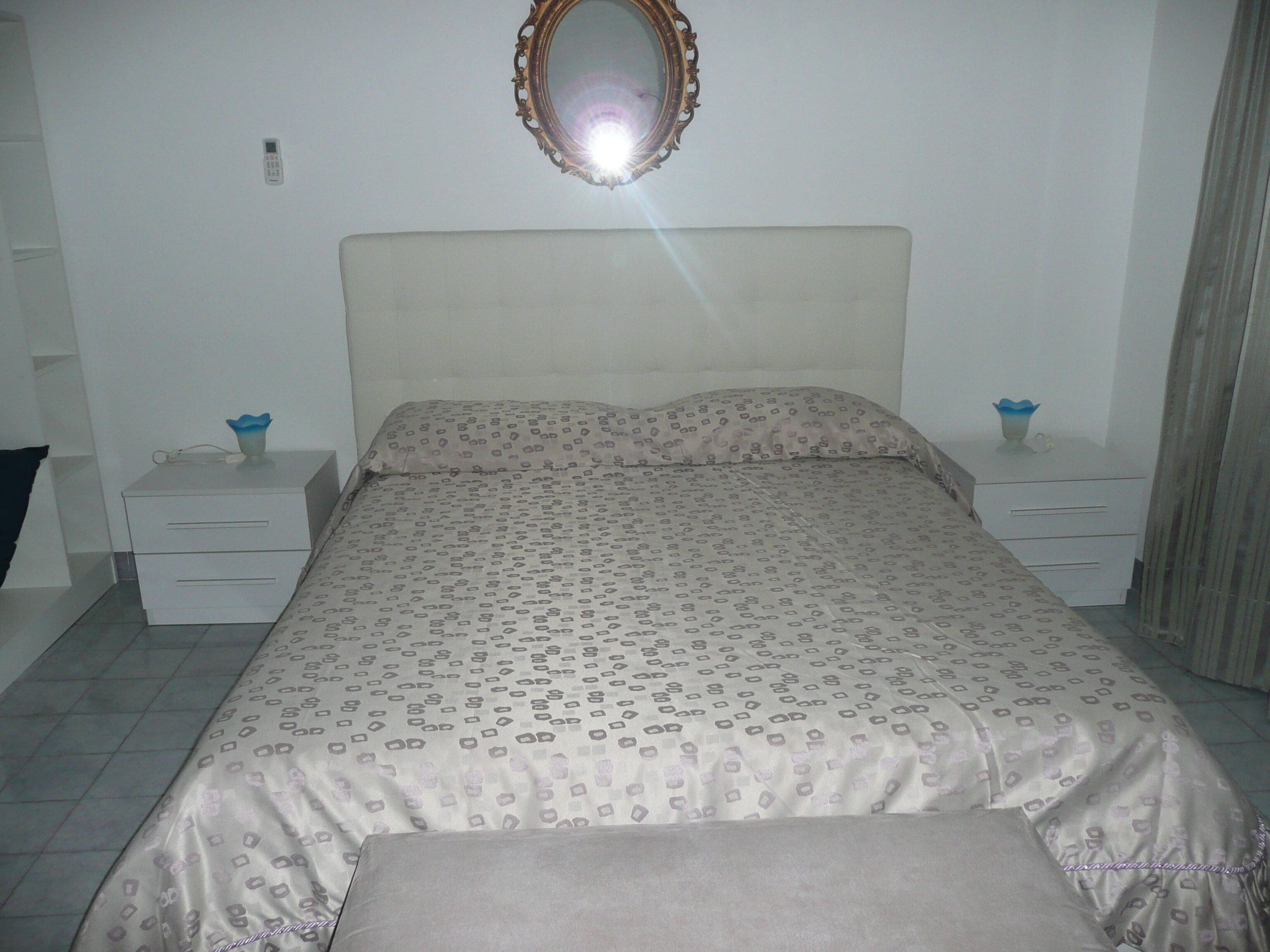 Un dormitorio con una cama, dos mesitas de noche, un espejo y una ventana con cortinas.