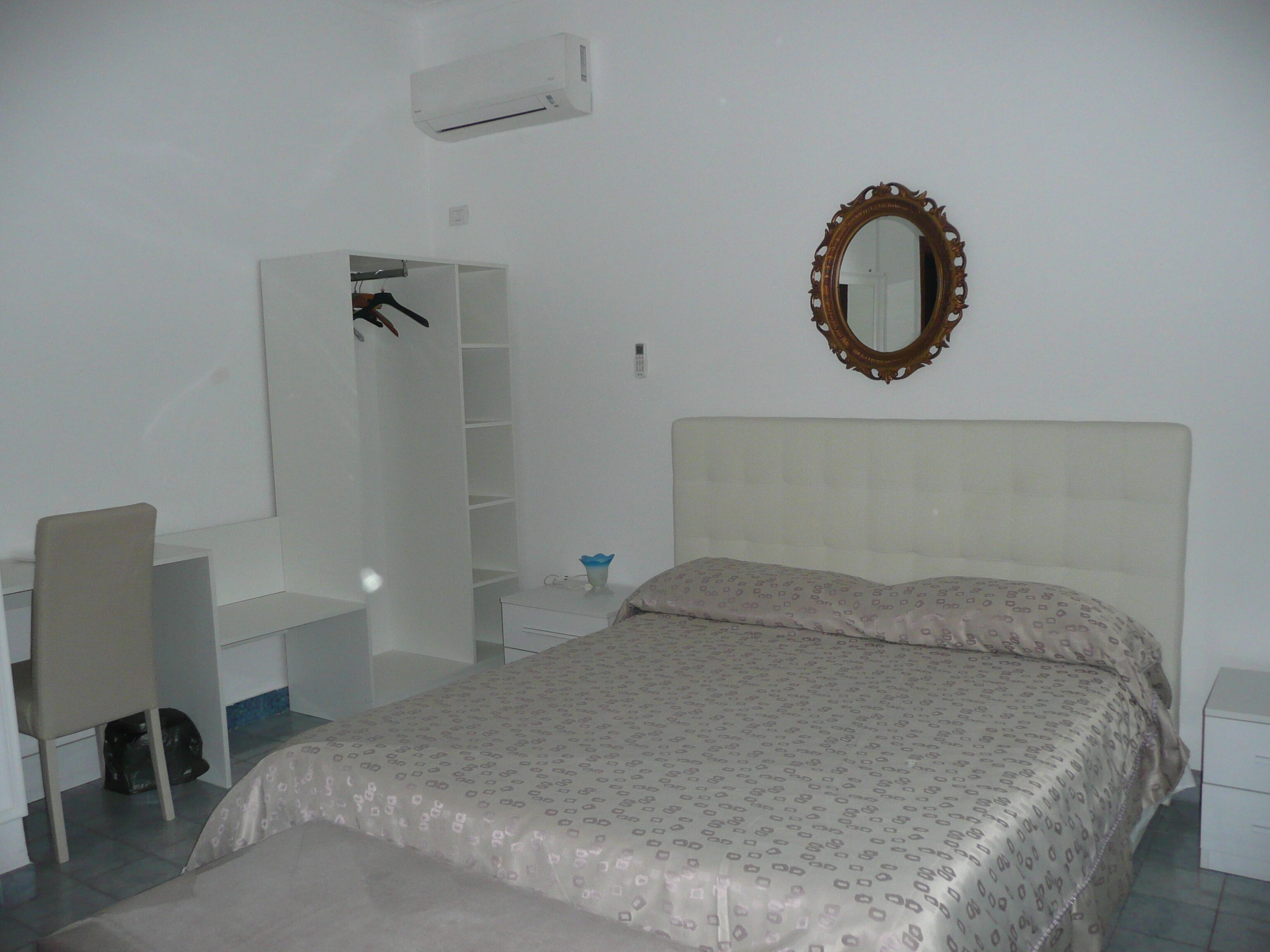 A bedroom with a bed, a desk, a chair, a wardrobe, and a mirror.