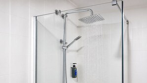 Une douche fermée par des parois en verre, équipée d’un pommeau de douche à main et d’un pommeau de douche fixe au plafond.