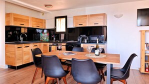 A modern kitchen with wooden cabinets, a dining table with chairs, and a flat-screen TV mounted on the wall. - Corsica seaside House n°5 Residence Saint Vincent Corse (Occhiatana)