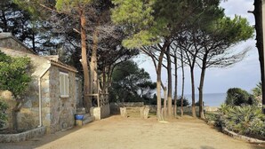 A rustic stone building with a wooden deck, surrounded by tall trees and a sandy ground. - Corsica seaside House n°5 Residence Saint Vincent Corse (Occhiatana)