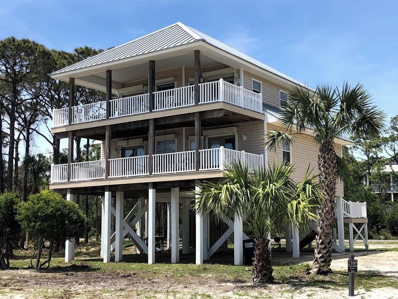 Une maison de deux étages située en bord de mer, dotée d’un balcon à chaque étage et soutenue par des piliers en bois.