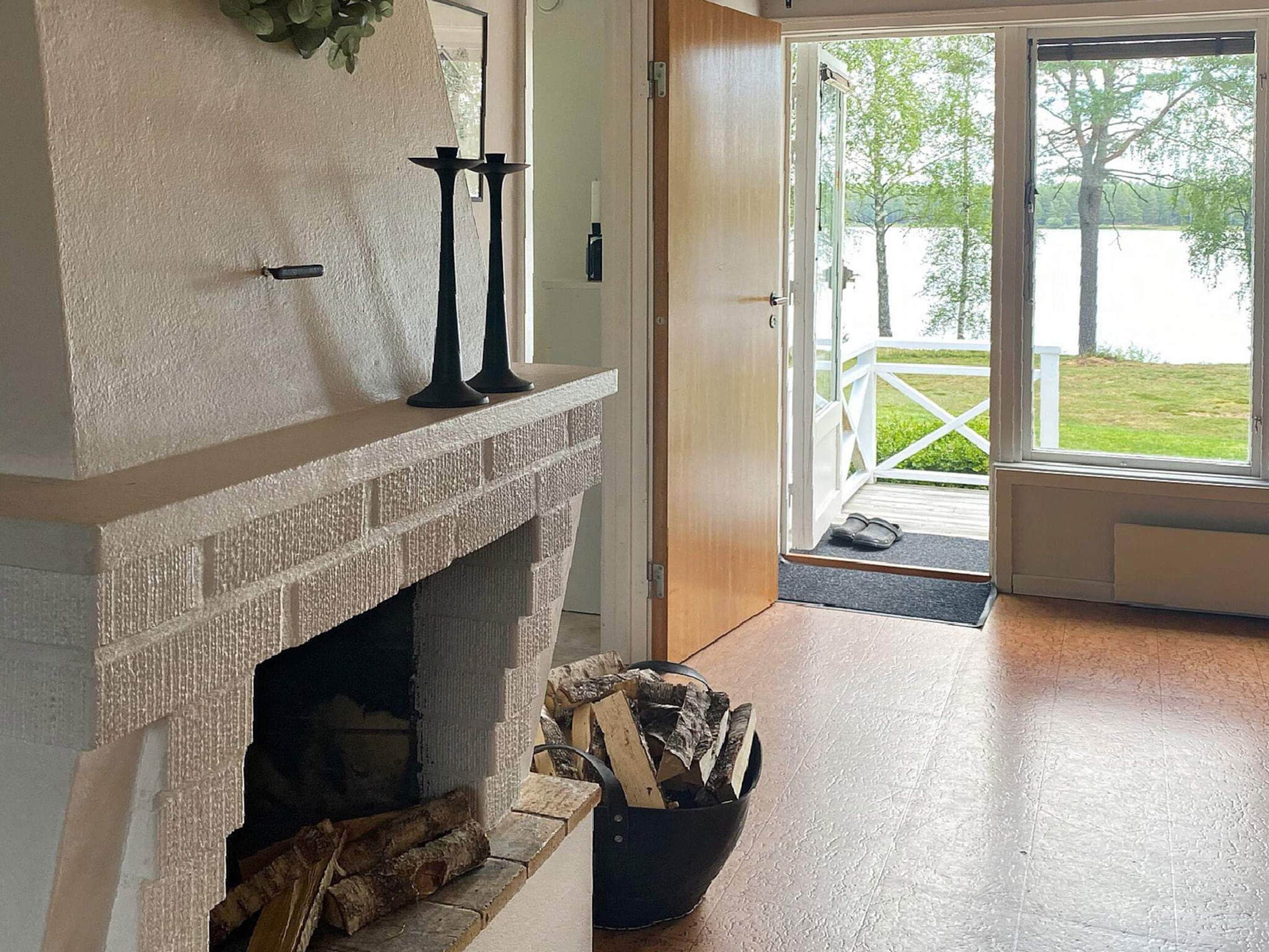 Una chimenea con repisa de piedra, un candelabro negro y una cesta de leña.