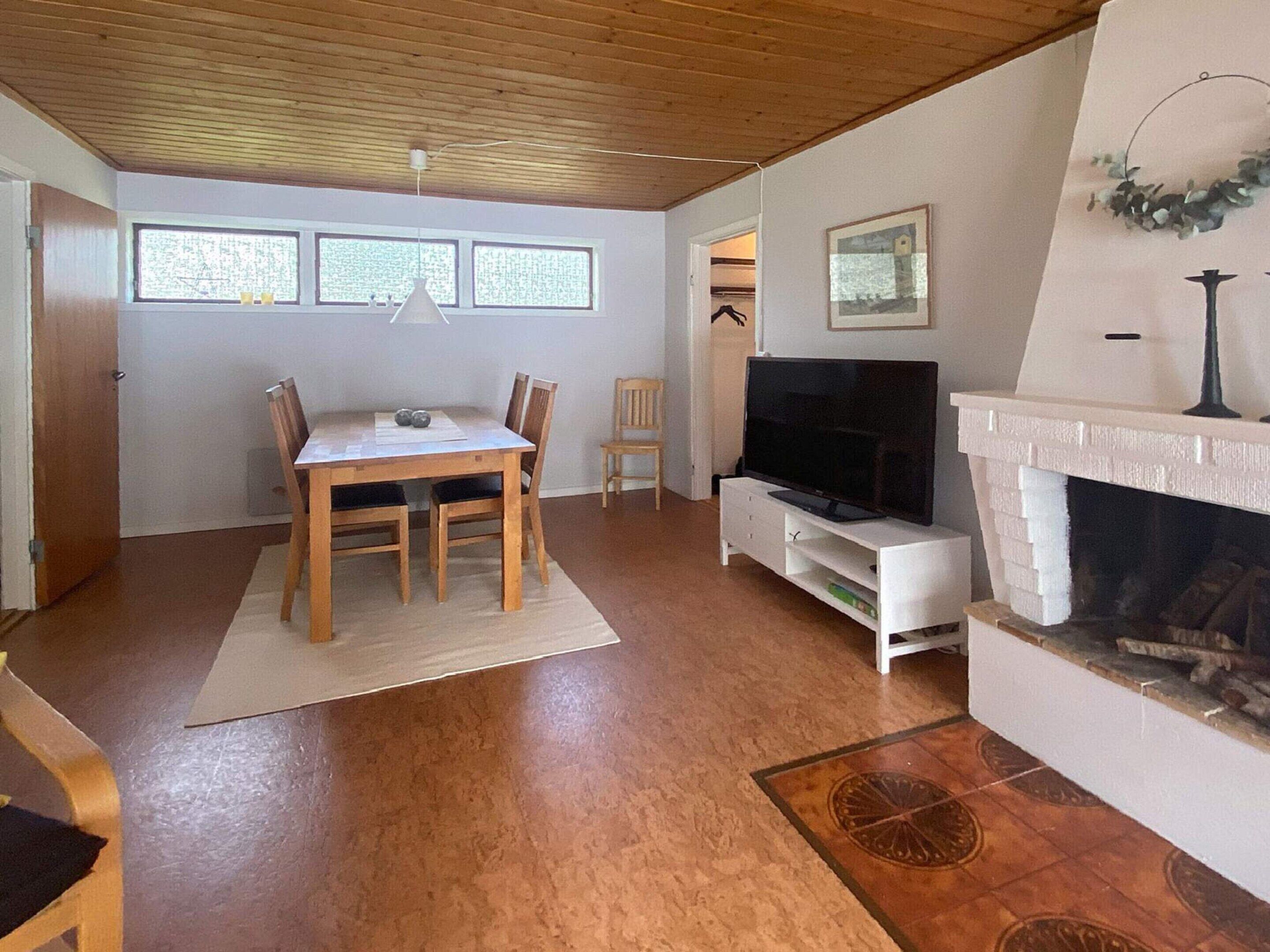 A living room with a wooden dining table, chairs, a flat-screen TV, a fireplace, and a large window with blinds.