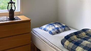 A bedroom with a bed, a wooden dresser, and a window.