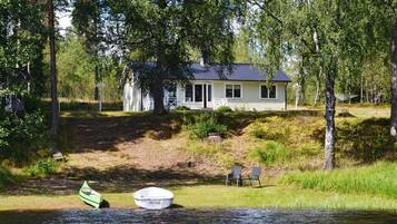A house with a dock and chairs by a calm body of water, surrounded by trees.