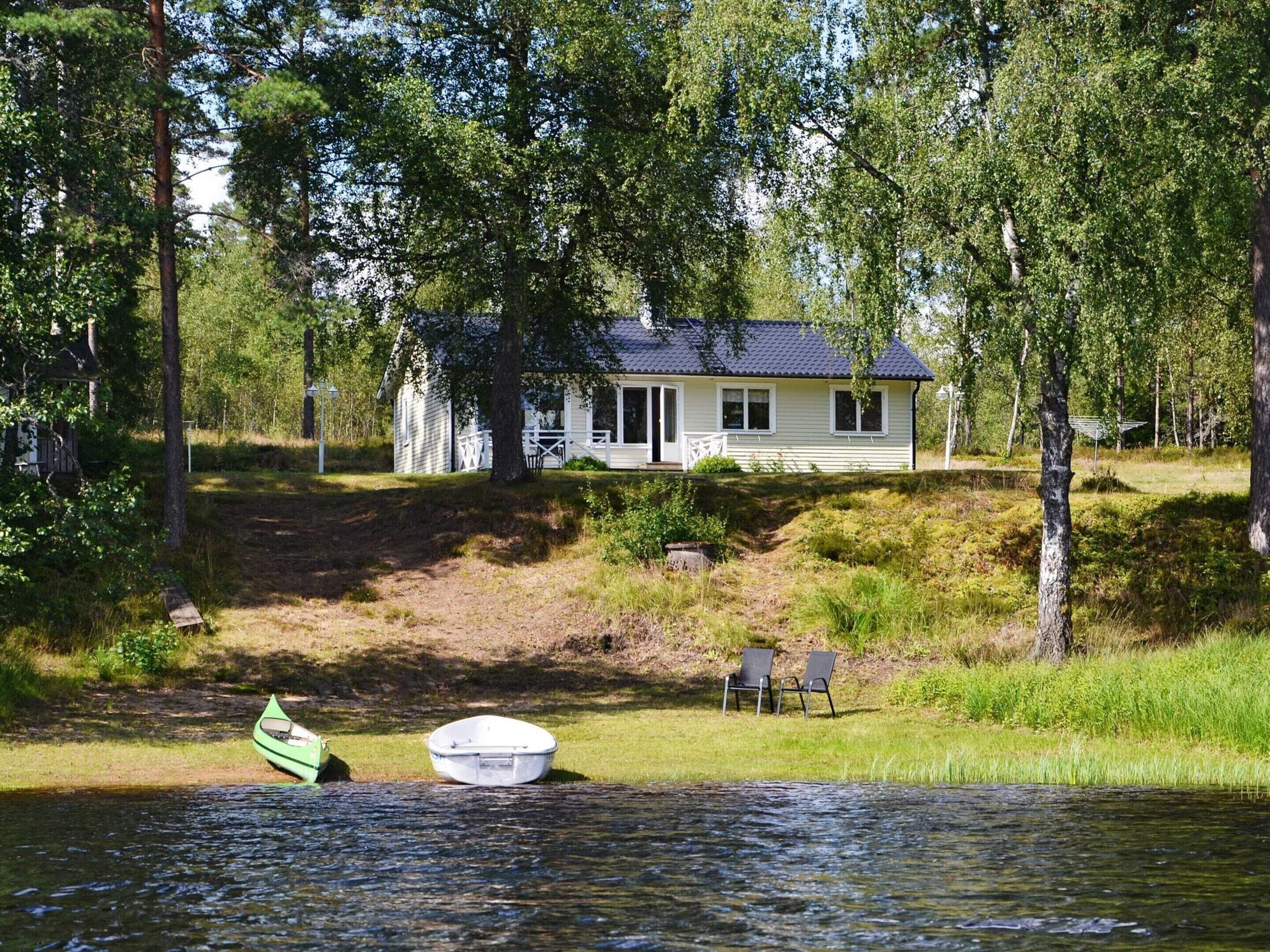 A house with a dock and chairs by a calm body of water, surrounded by trees.