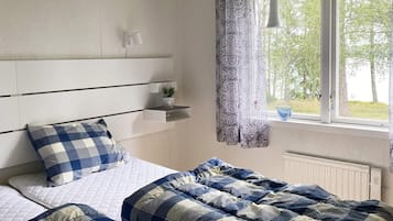 A bedroom with a bed, a bedside table, a window with curtains, and a view of trees.
