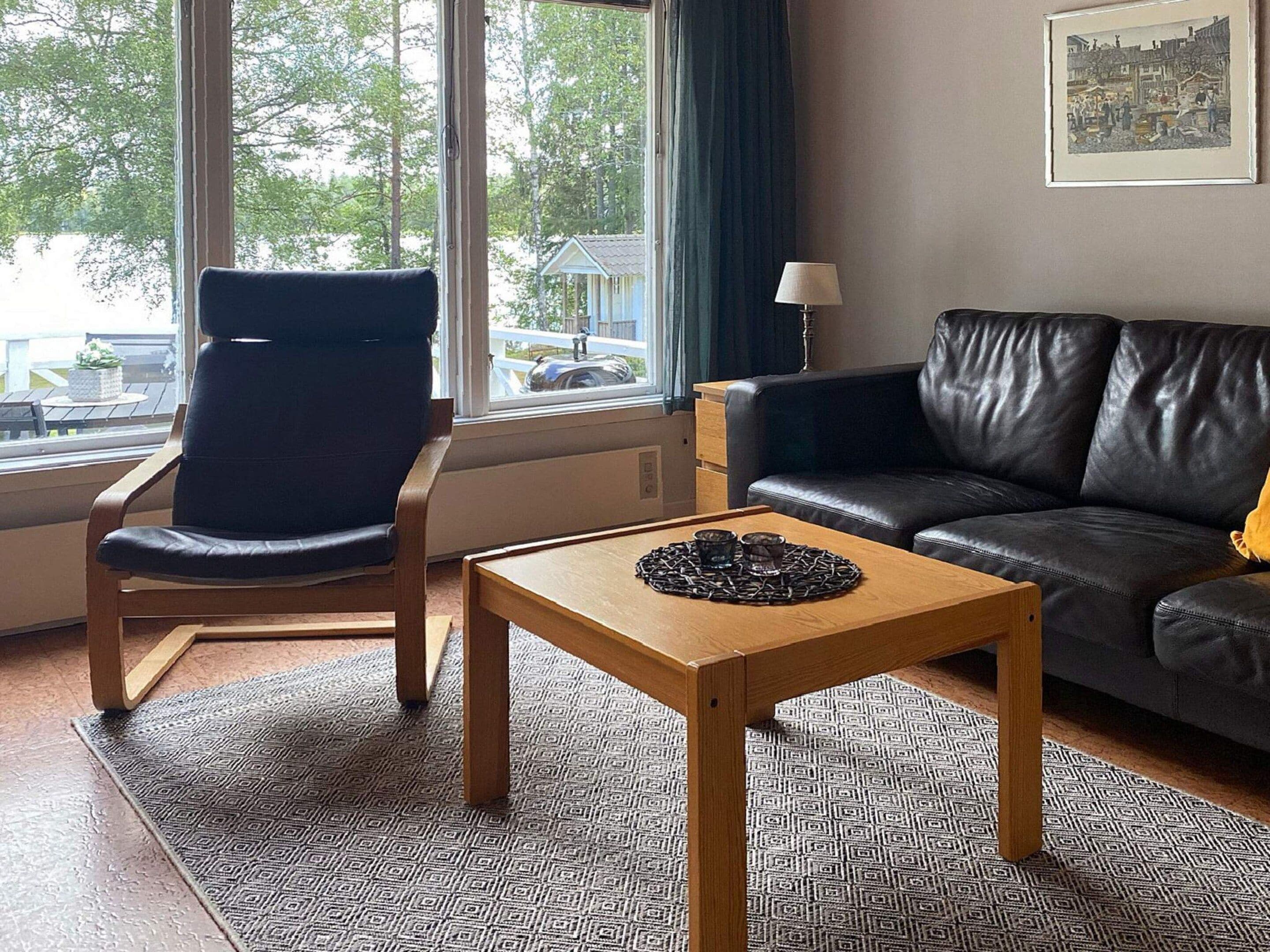 A living room with a leather sofa, a wooden coffee table, a black chair, and a window with a view of a building and trees.