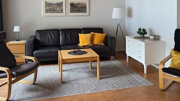 A modern living room with a black leather sofa, wooden coffee table, and a white dresser.