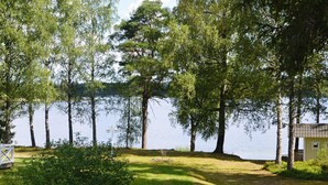 A lakeside property with a grassy area, a small shed, and a row of trees. - 4 Star Holiday Home in Gislaved (Gislaved)
