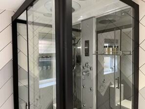 A modern bathroom with a glass-enclosed shower, a control panel, and a shelf with toiletries.