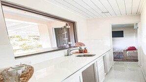 A modern kitchen with a large window, a sink, and a dining area visible through the doorway.