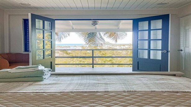 A room with a bed, a view of the beach, and a blue door.