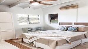 A bedroom with a bed, ceiling fan, air conditioning unit, and two windows with blinds.